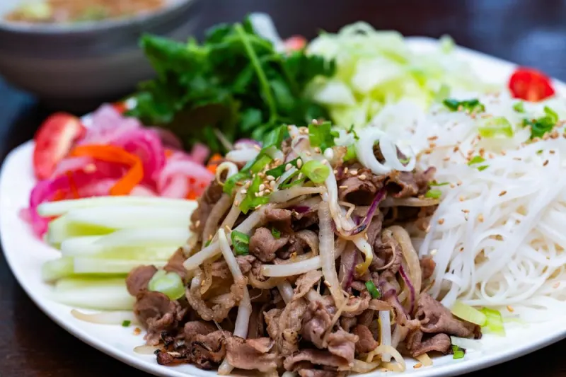 Bún chả platter of smoky beef belly with rice noodles, cucumber, tomatoes, and herbs