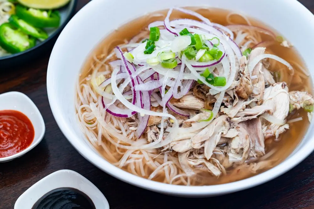 Chicken phở with hand-pulled chicken, red onion, and scallions, with sriracha and hoisin on the side