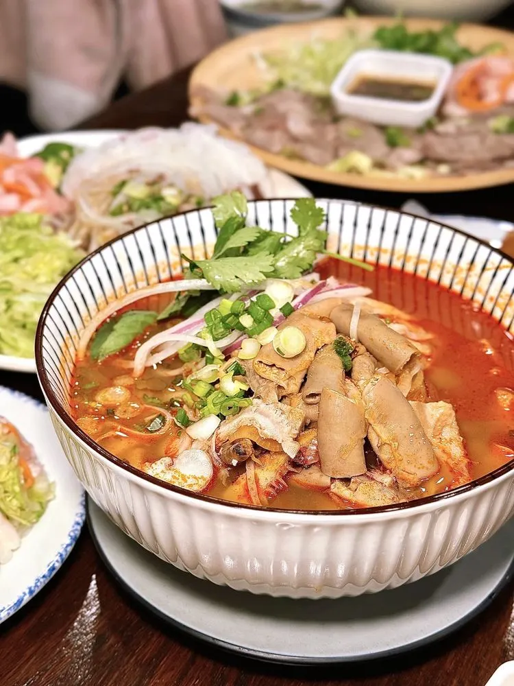 Red lemongrass spicy phở with intestines, herbs, and scallions in a white ribbed bowl